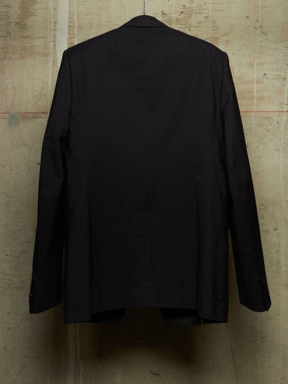 A black pinstripe suit jacket hanging on a hanger against a textured concrete wall, showing the back view.