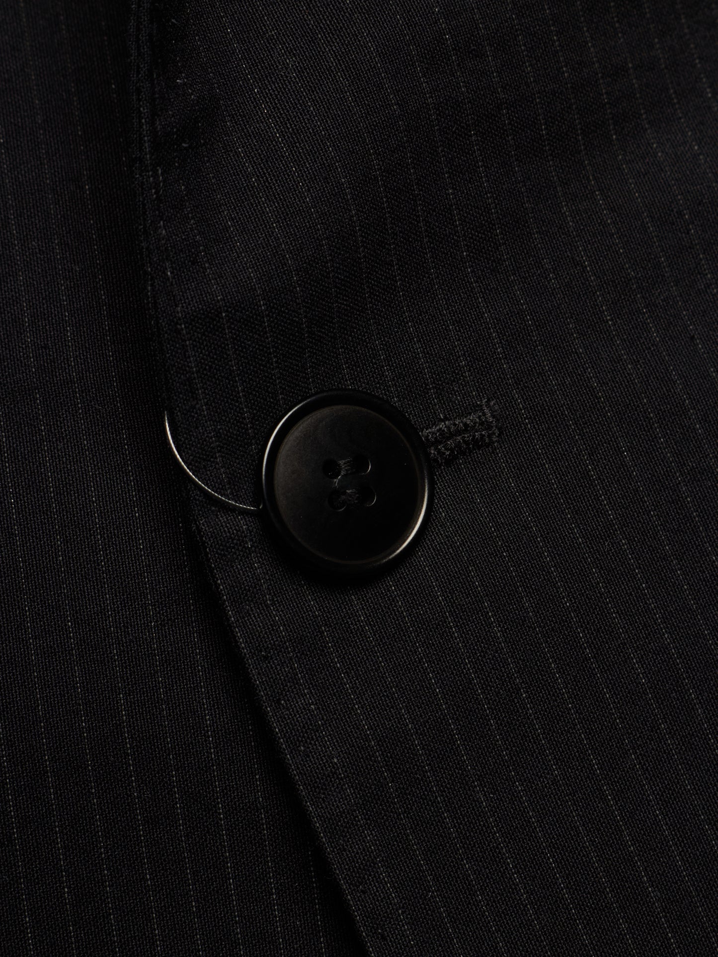 Close-up of a black pinstriped blazer fabric with a black button detail.
