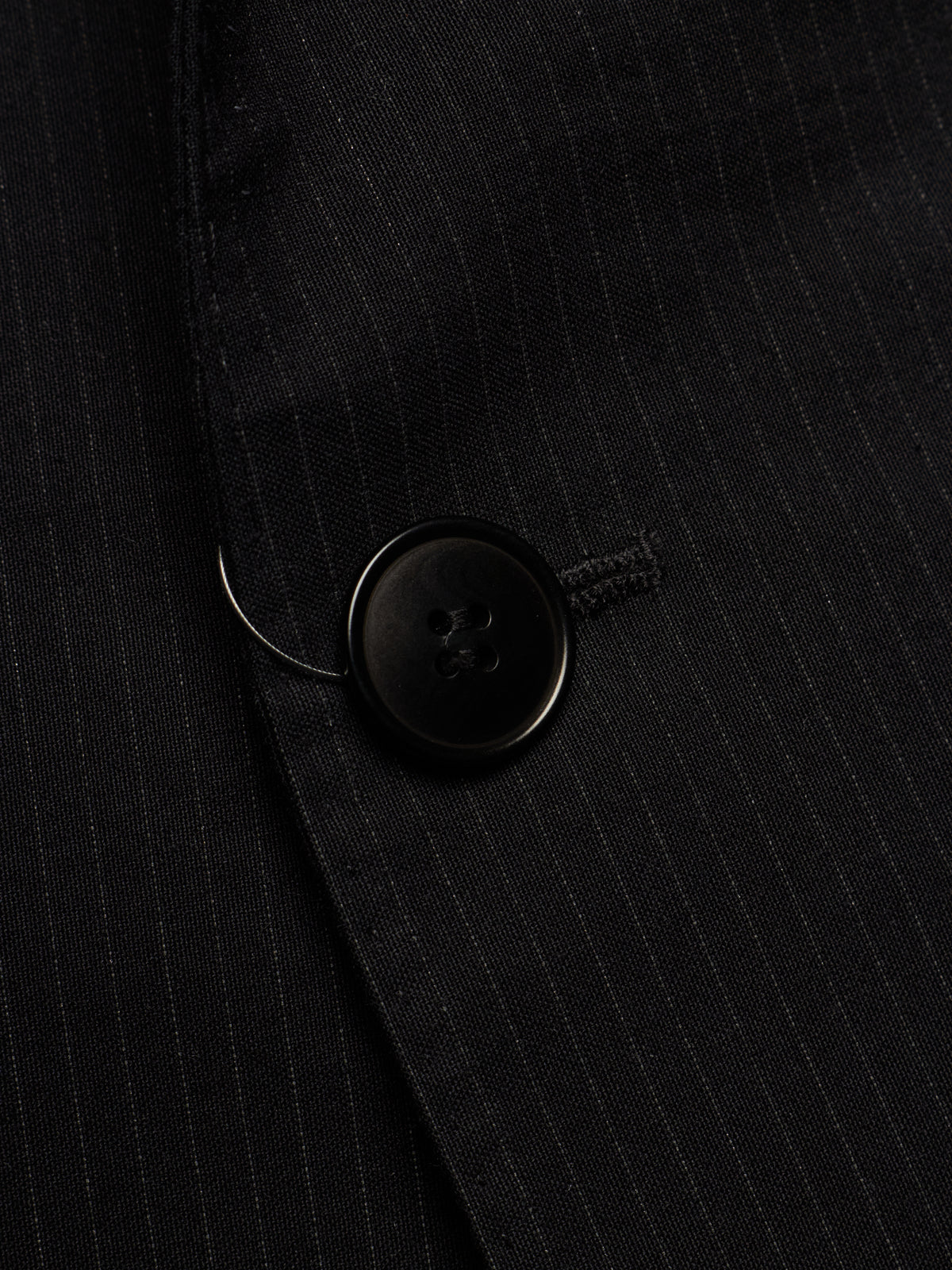 Close-up of a black pinstriped blazer fabric with a black button detail.
