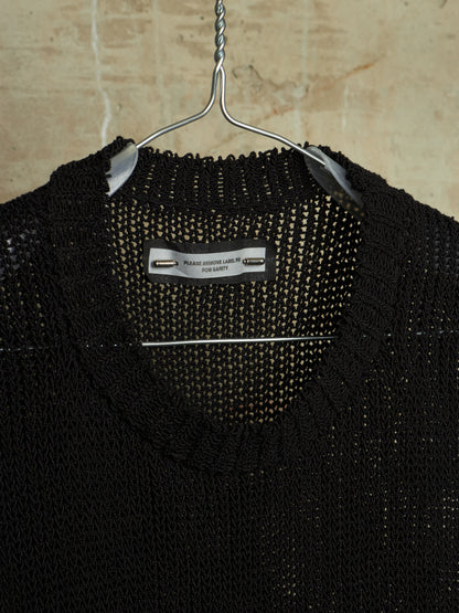A close-up of a black knit sweater hanging on a metal hanger against a beige stone wall. The inner neck label reads 'PERRY FASHION LABEL LTD FOR LATE'.