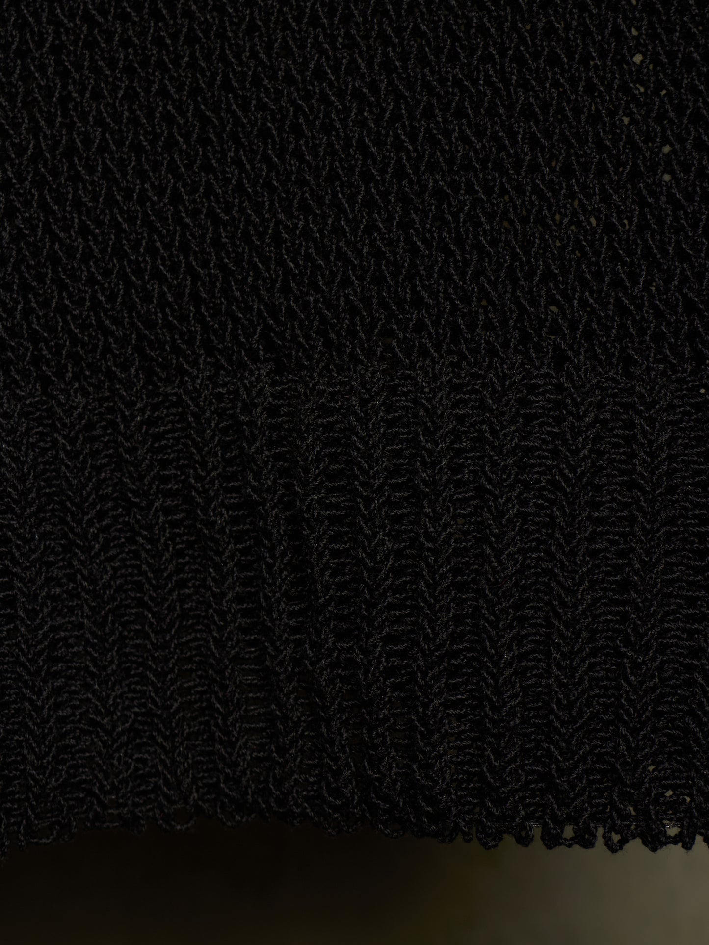 Close-up of a black textured knit fabric with a ribbed hem, showing the detailed weave and fringe edge.