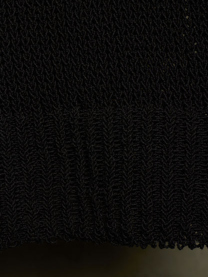 Close-up of a black textured knit fabric with a ribbed hem, showing the detailed weave and fringe edge.