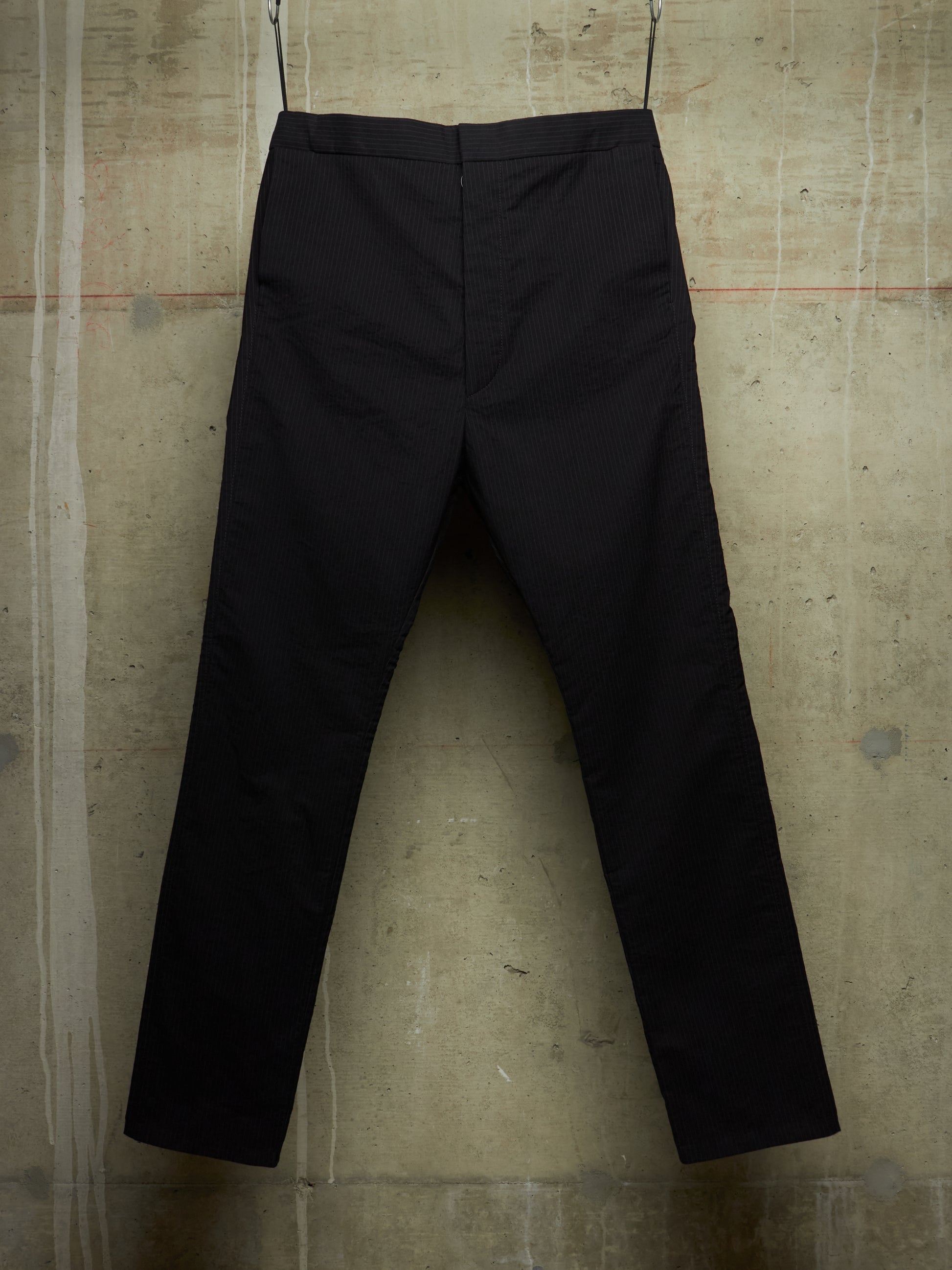 Black trousers hanging against a textured concrete wall.