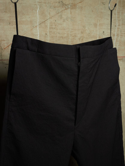 Black pinstriped trousers hanging from metal hooks against a textured beige wall.