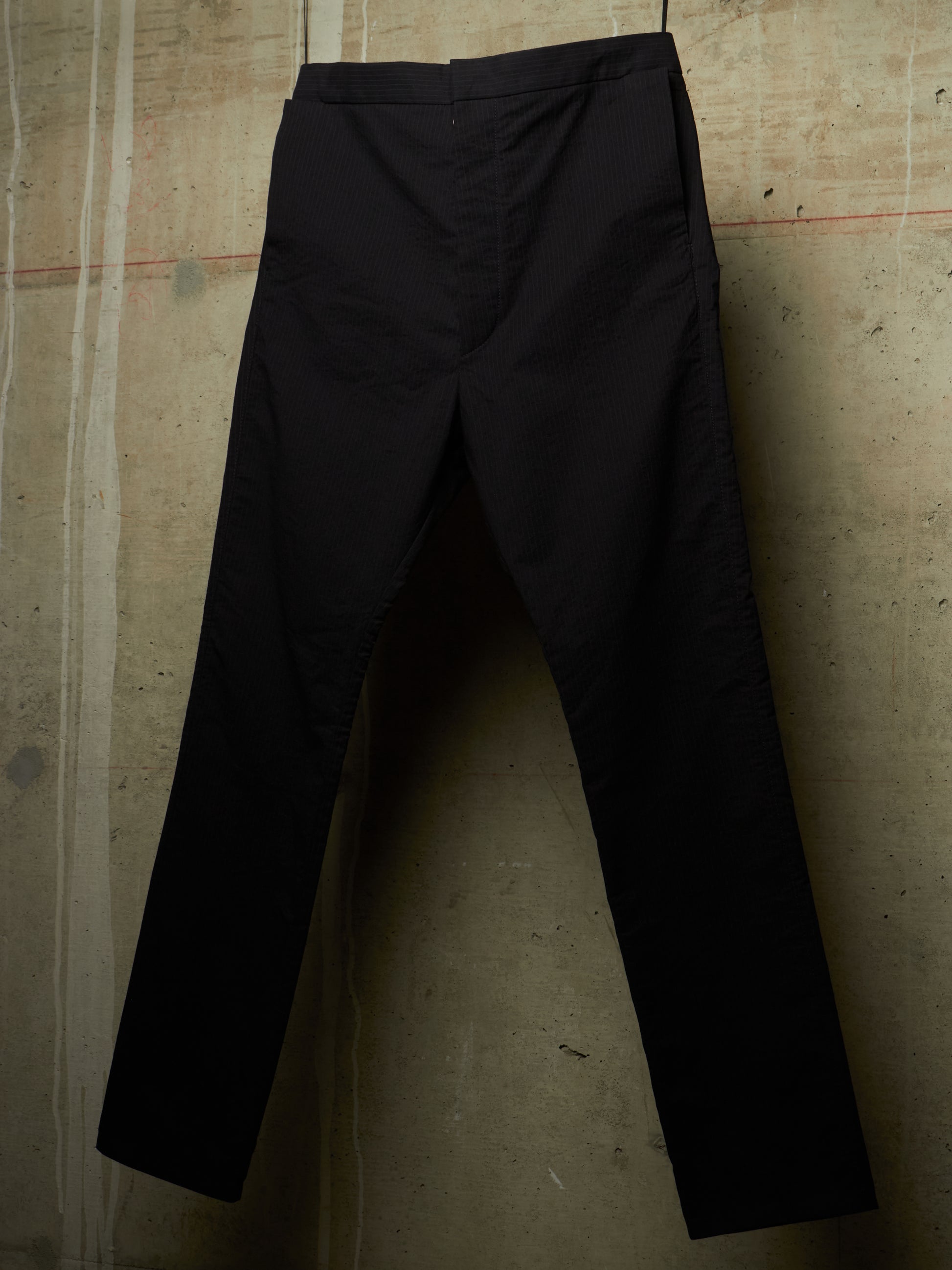 Black slim-fit trousers hanging against a textured concrete wall.