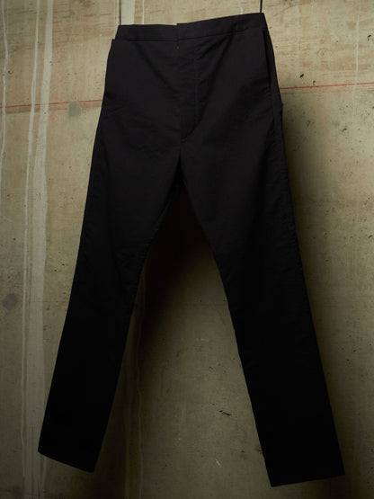 Black slim-fit trousers hanging against a textured concrete wall.