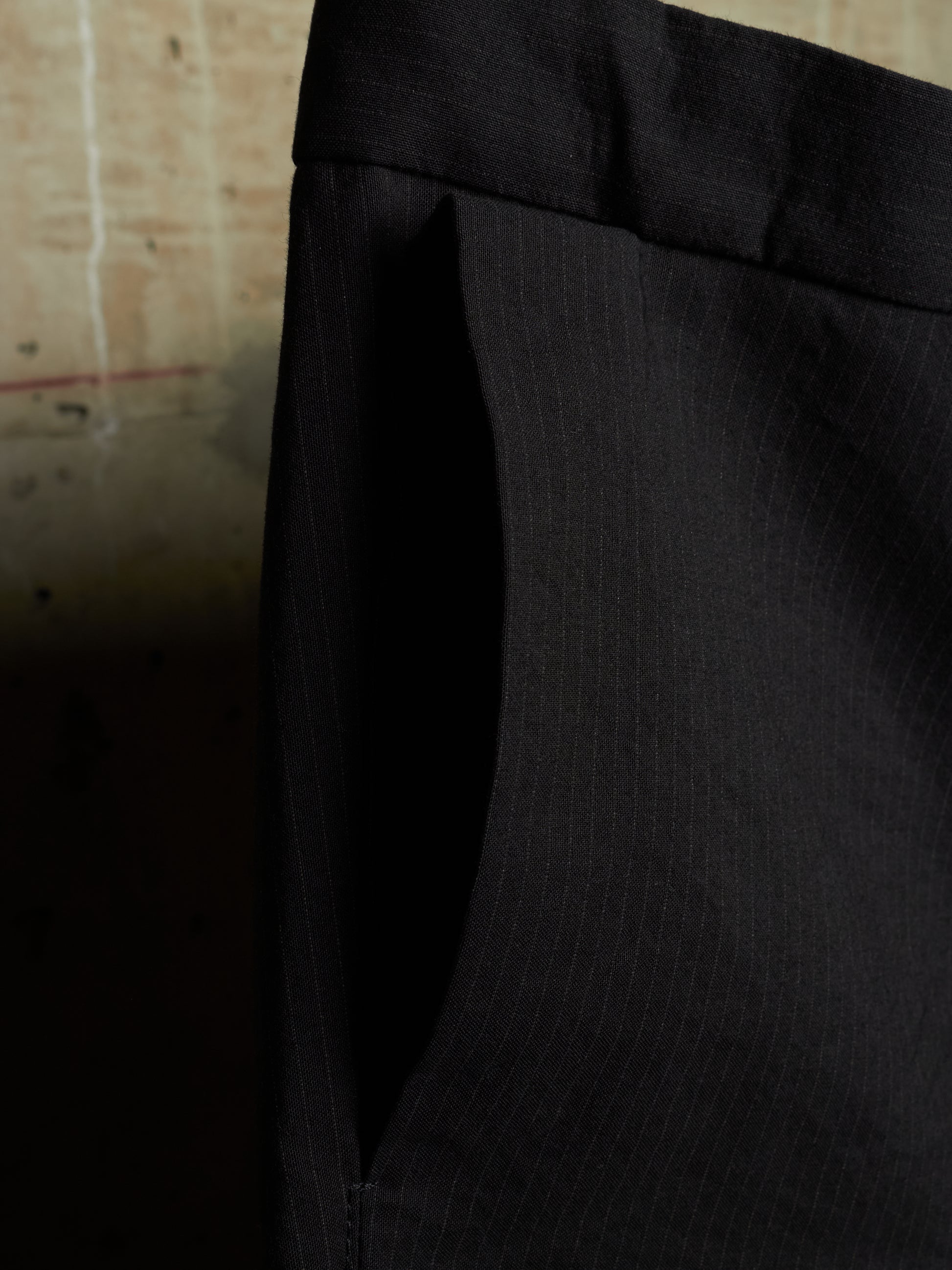 Close-up of a black pinstriped fabric garment, showing the texture and waistband detail against a dark background.