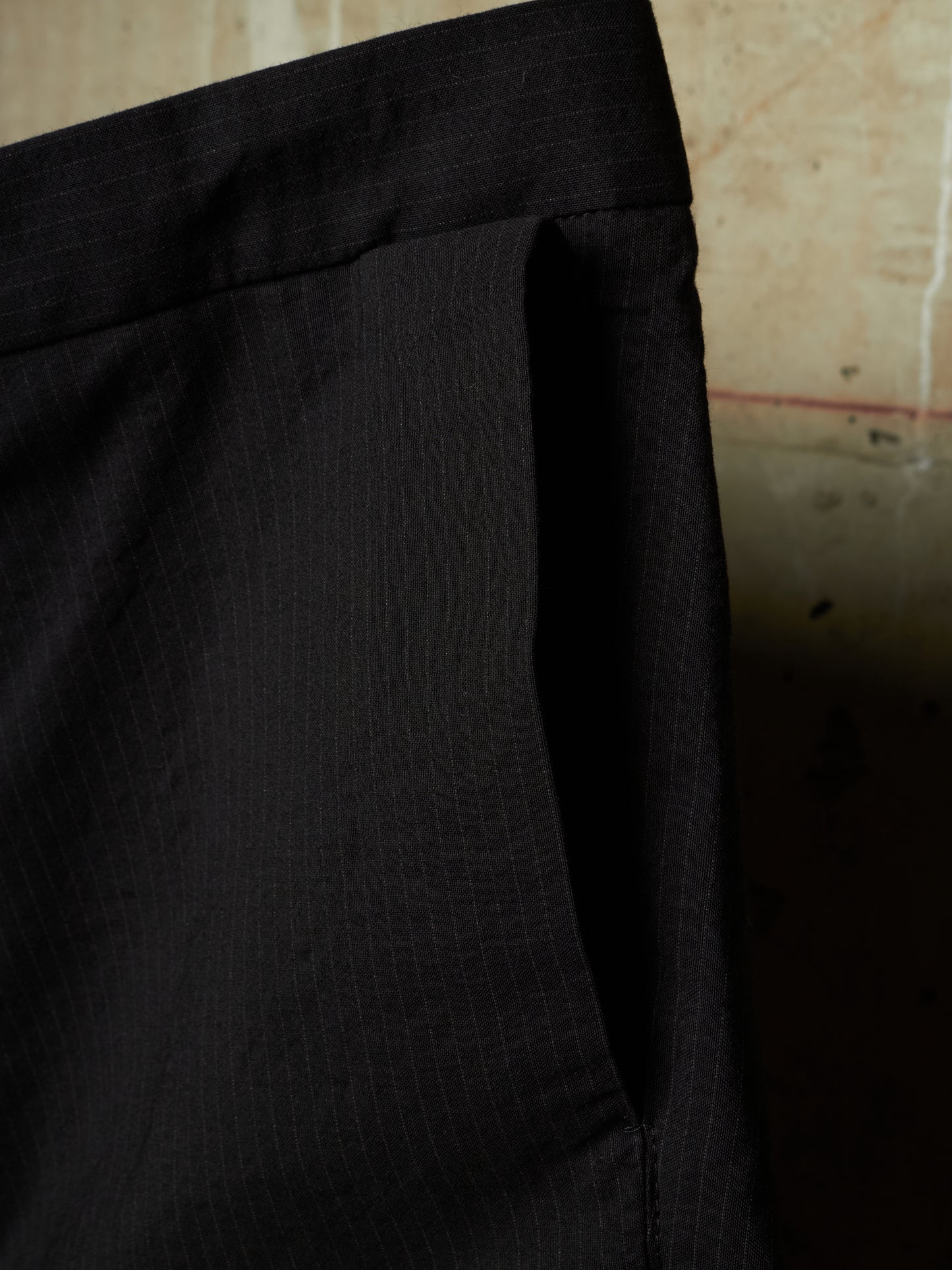 Close-up of black pinstriped trousers showing the waistband and side pocket detail against a neutral background.