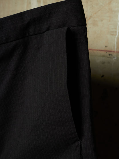 Close-up of black pinstriped trousers showing the waistband and side pocket detail against a neutral background.