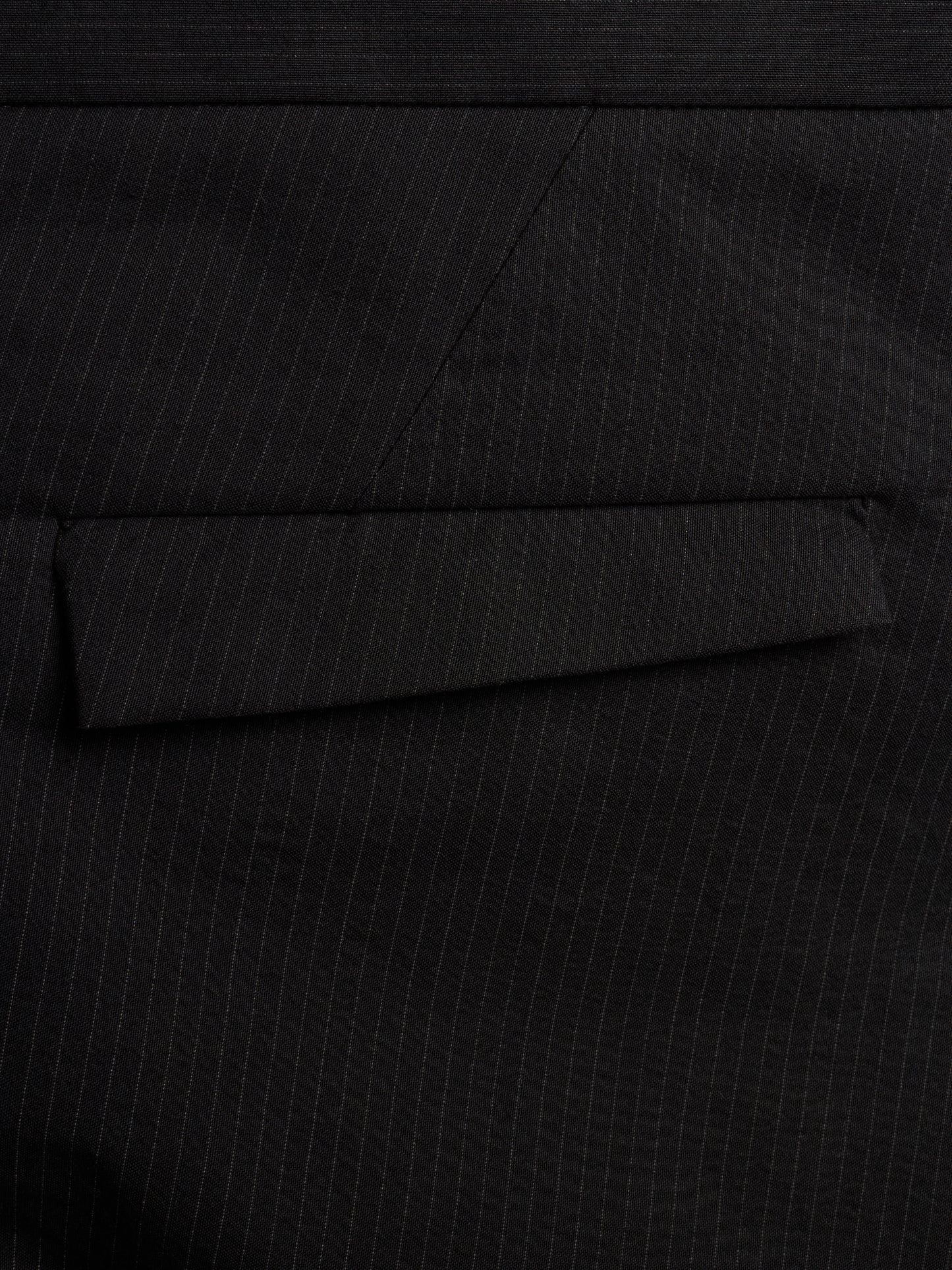 Close-up of a black pinstripe fabric surface with a folded pocket flap visible.