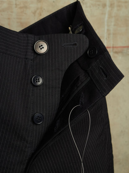 Close-up of a black pinstriped shirt jacket showing the collar, button closure, and thread against a textured beige background.