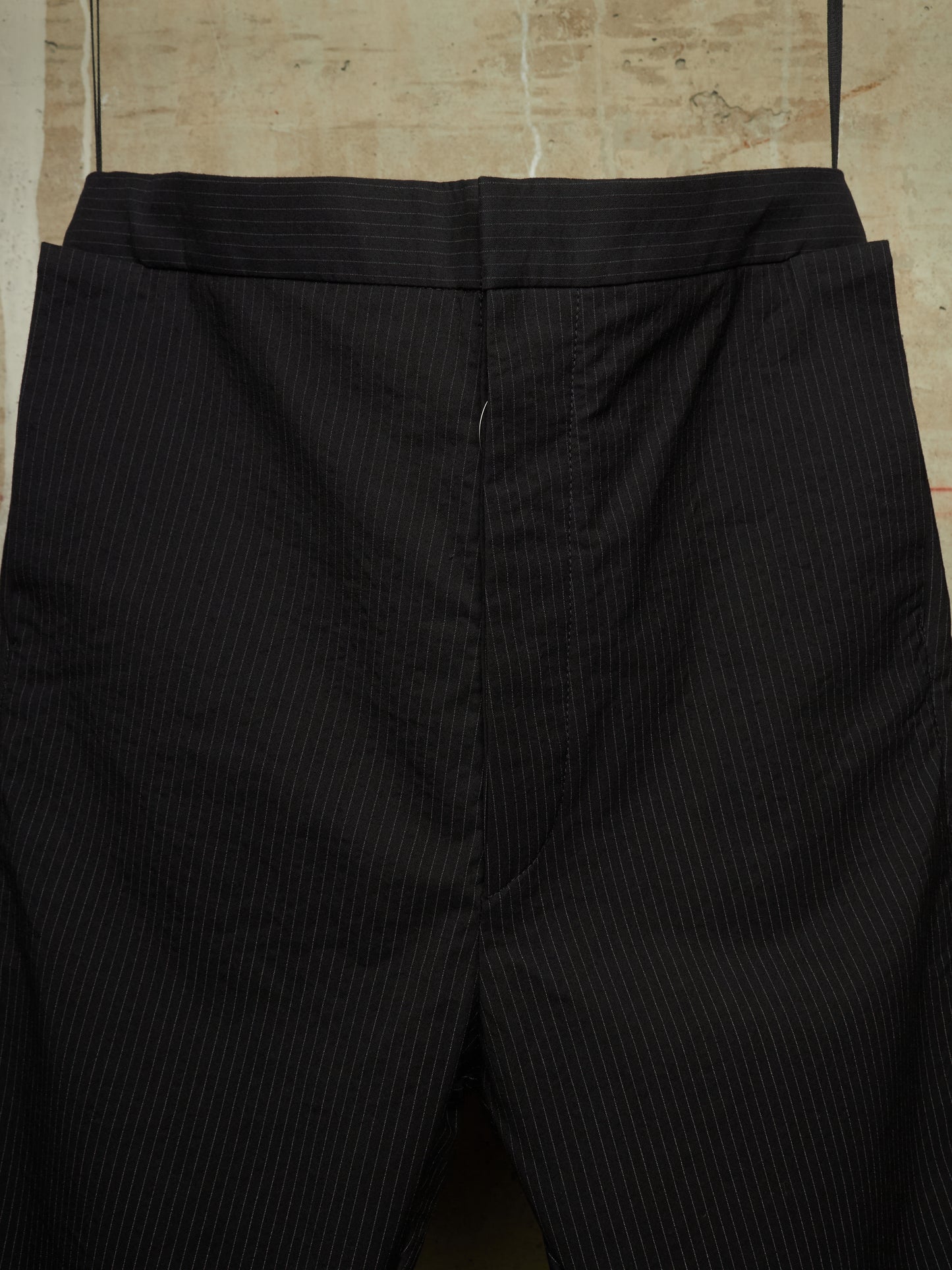 Black pinstriped trousers hanging against a beige tiled wall.