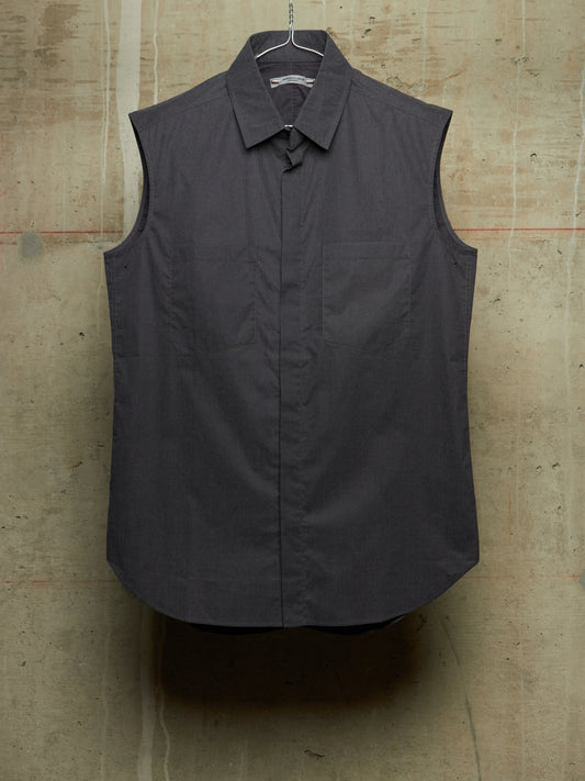 A dark charcoal gray sleeveless button-up shirt with a pointed collar and chest pocket, hanging on a wire hanger against a textured concrete wall.