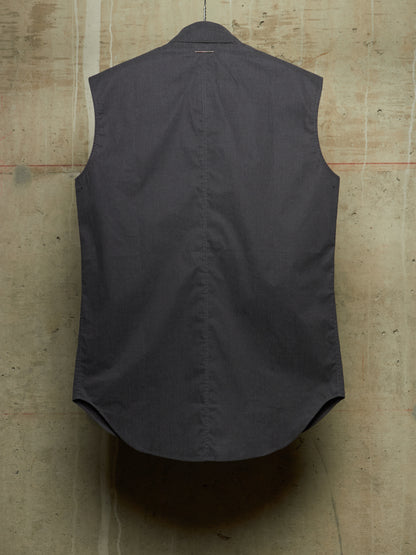 A dark charcoal gray sleeveless vest shown from the back, hanging against a textured concrete wall.