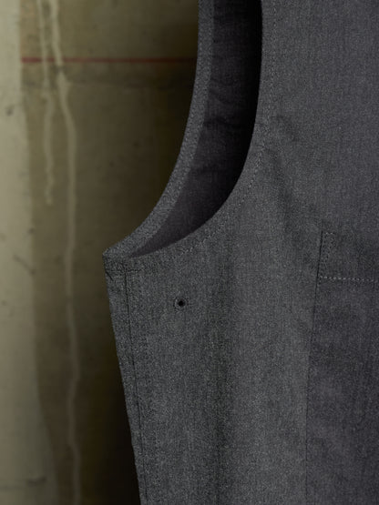 Close-up detail shot of a dark gray textured fabric garment, showing the inner lining, curved neckline, and a small button detail against a neutral concrete background.