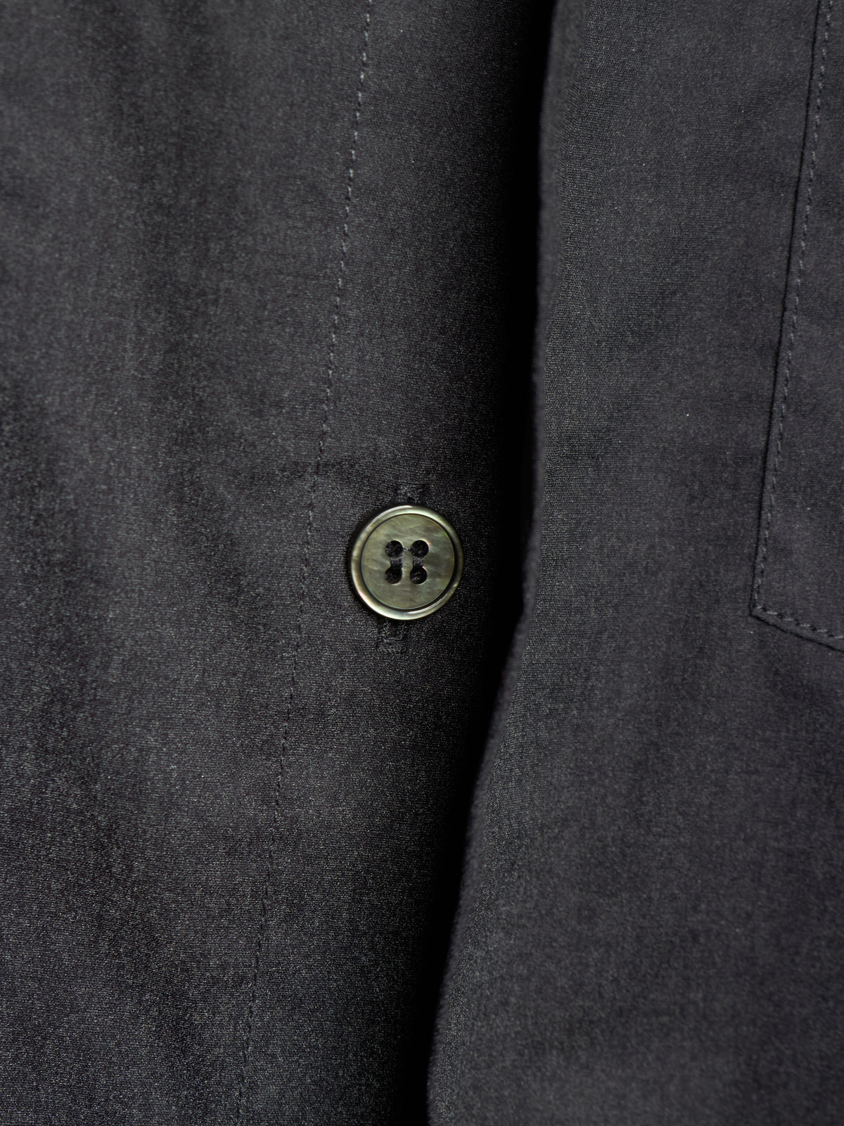 Close-up of a dark charcoal gray fabric jacket or coat with a single round metallic button on the front.
