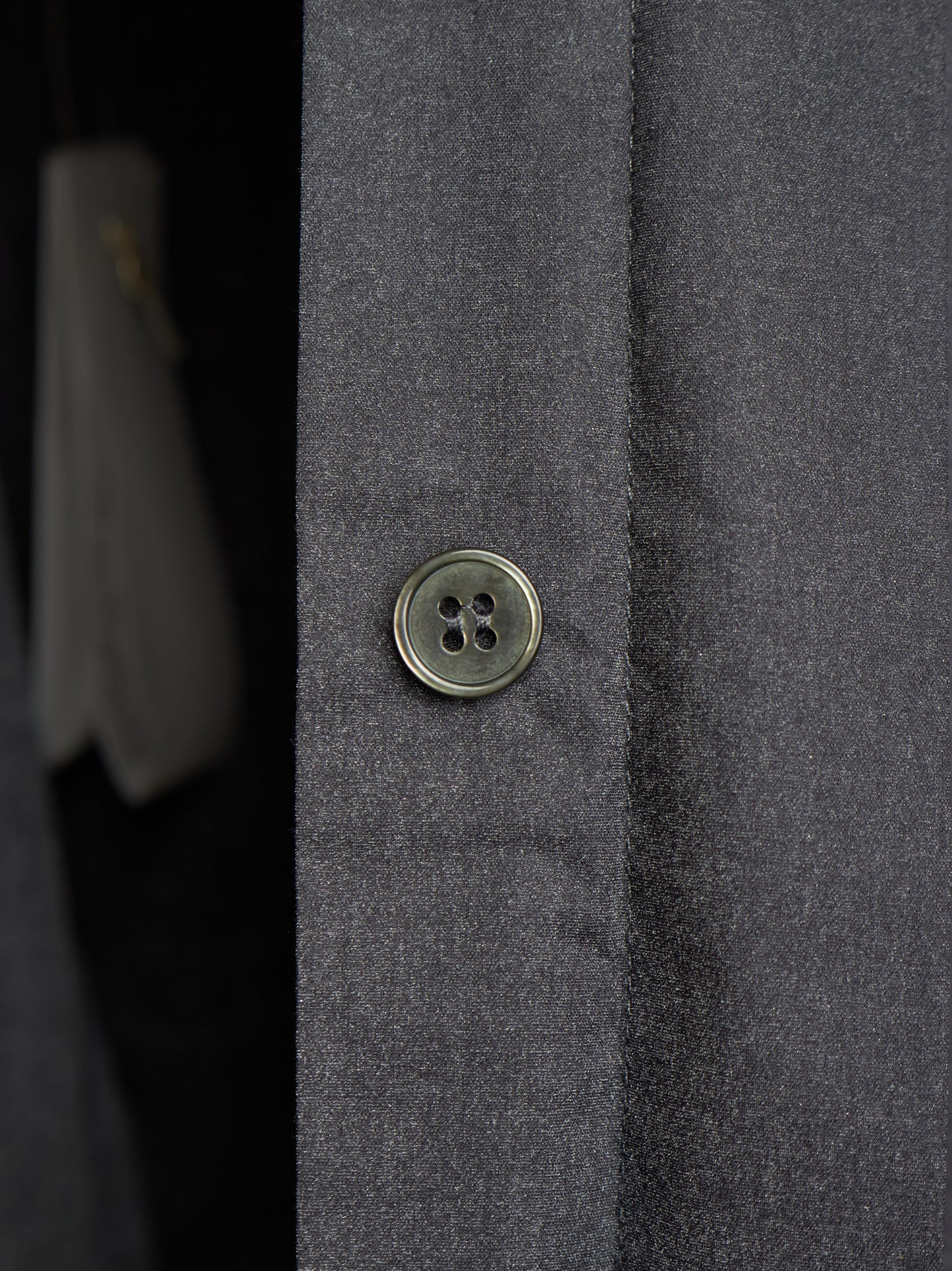 Close-up of a dark gray textured fabric garment with a single round metallic button on the front.