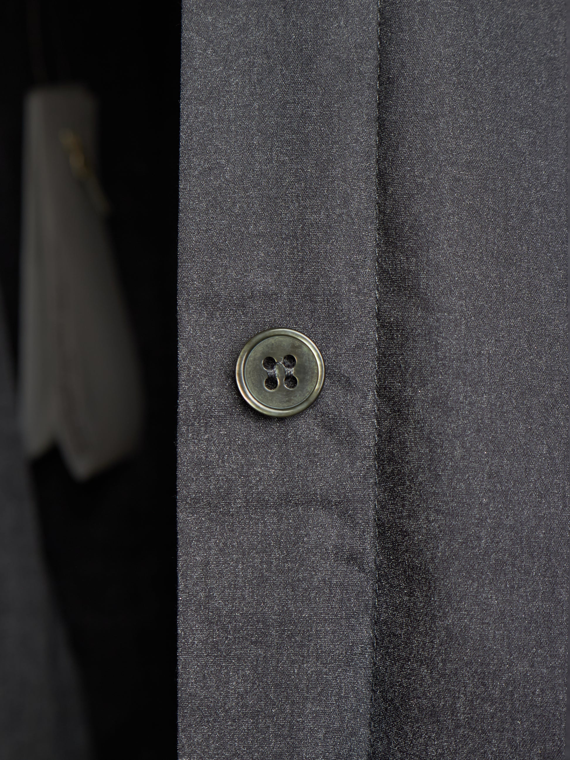 Close-up of a dark gray textured fabric garment with a single round metallic button on the front.