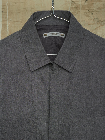 A dark gray textured collared shirt jacket hanging on a metal hanger against a rustic beige stone wall background.