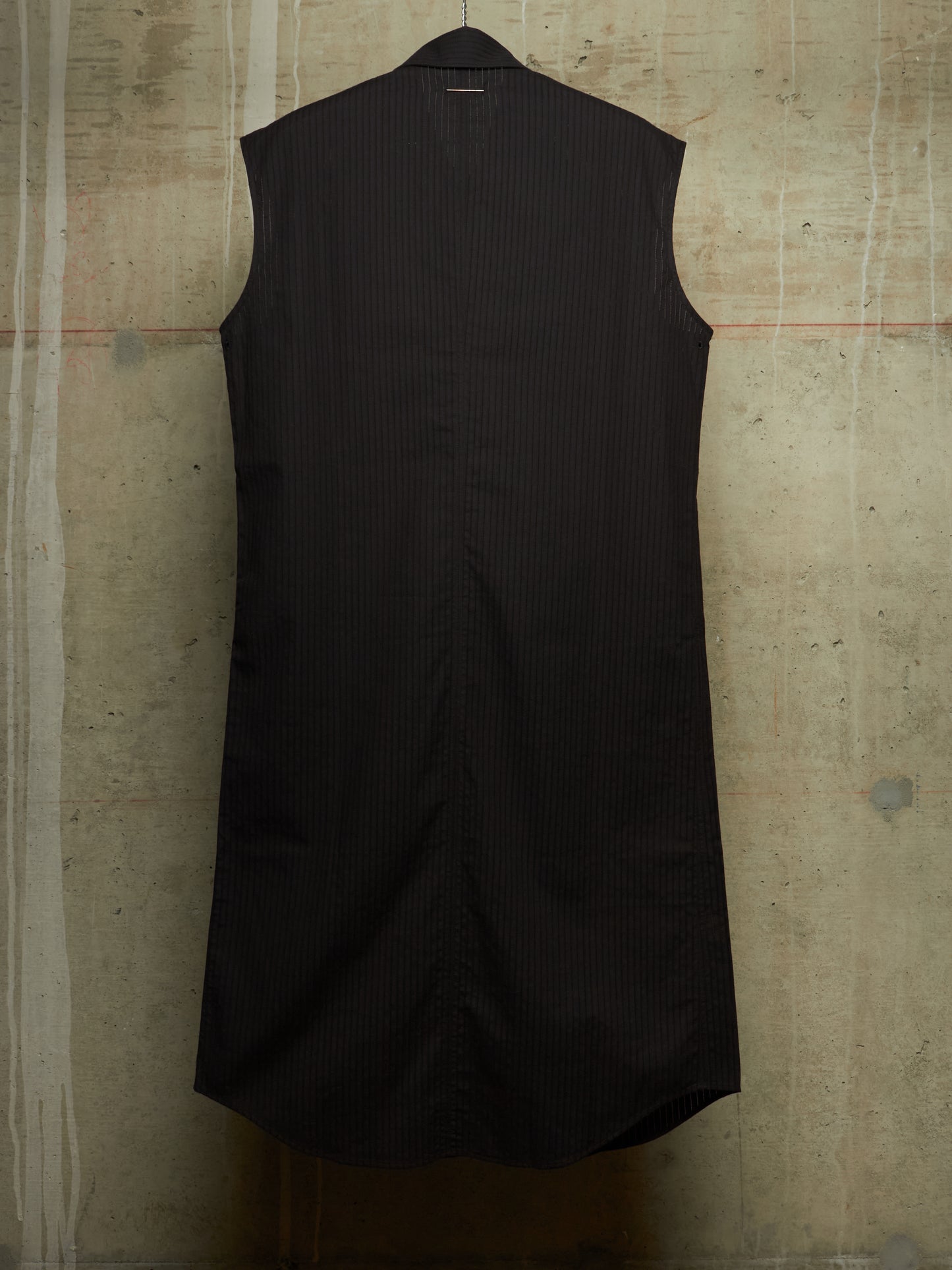 A sleeveless black pinstriped shirt dress hanging against a textured concrete wall.