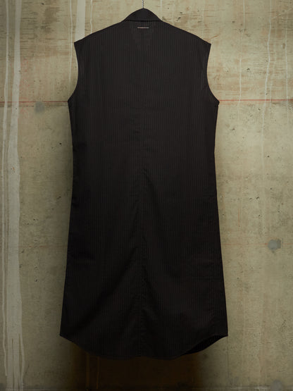 A sleeveless black pinstriped shirt dress hanging against a textured concrete wall.