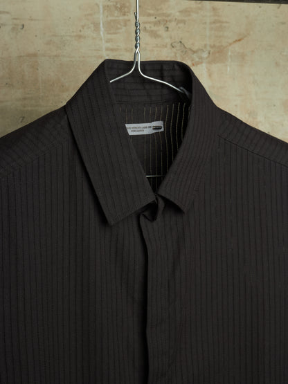 A dark brown pinstriped shirt hanging on a metal hanger against a textured beige stone wall.