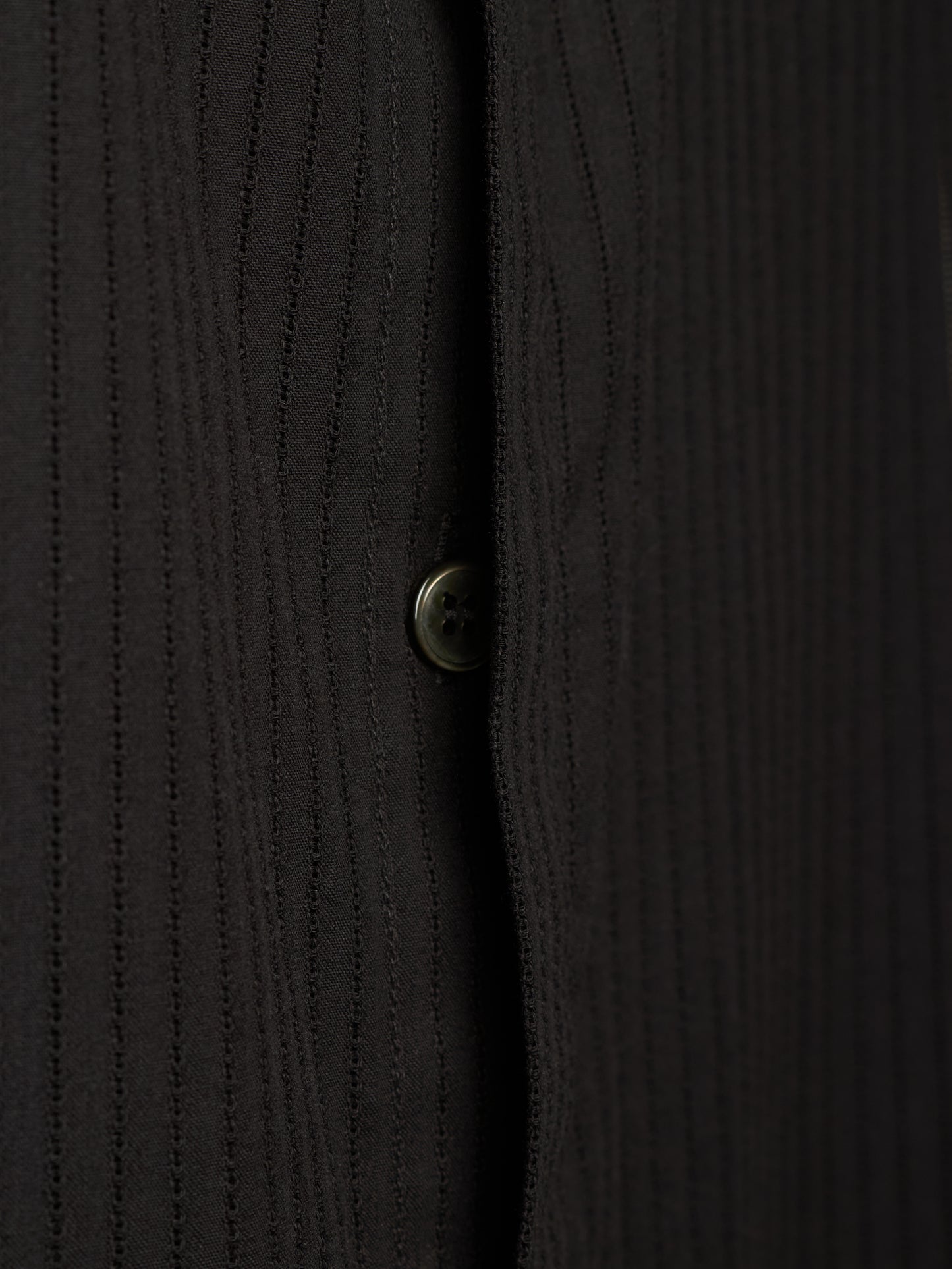 Close-up of a black ribbed knit button-up shirt showing the vertical texture and a single button.