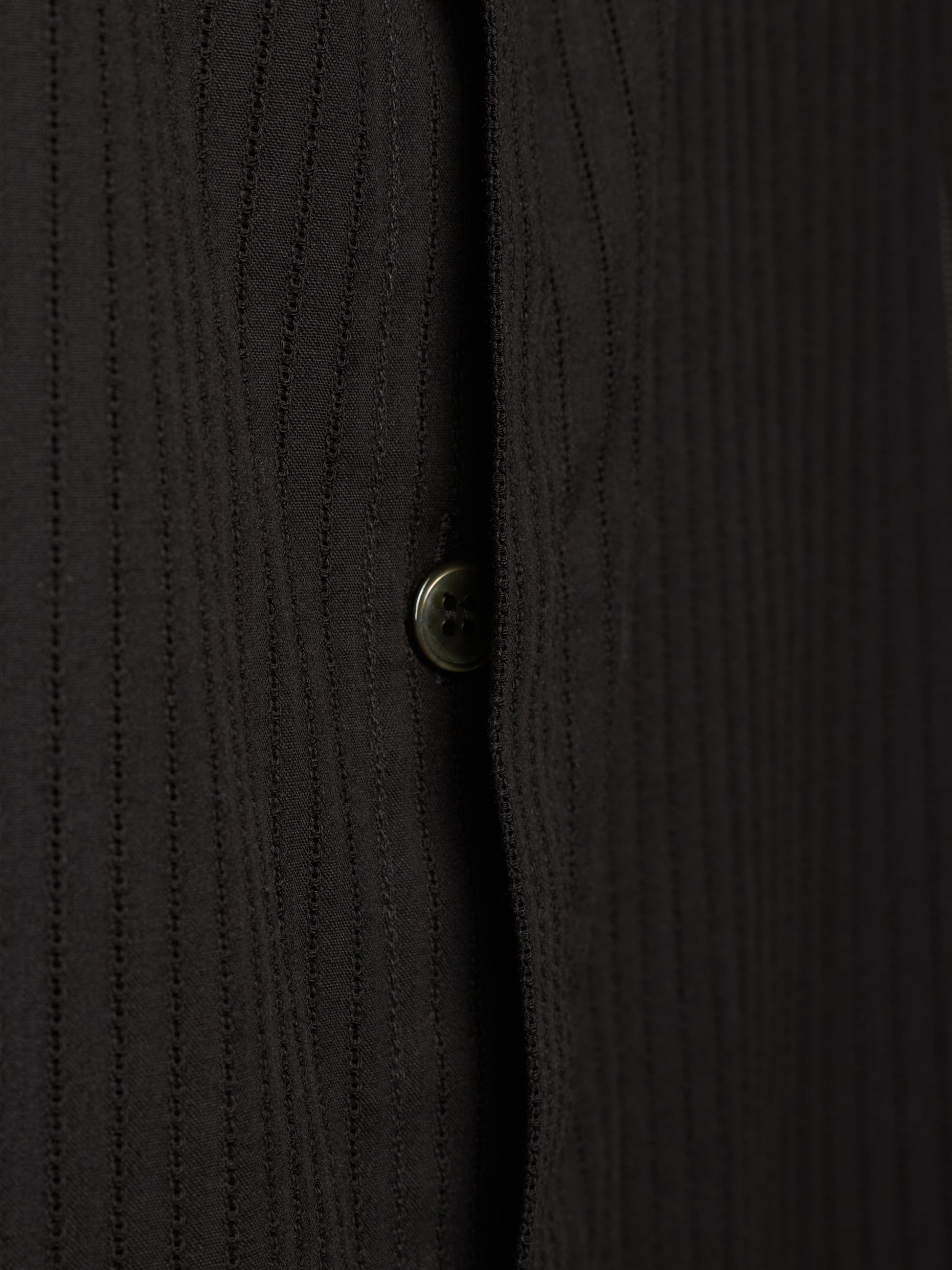 Close-up of a black ribbed knit button-up shirt showing the vertical texture and a single button.
