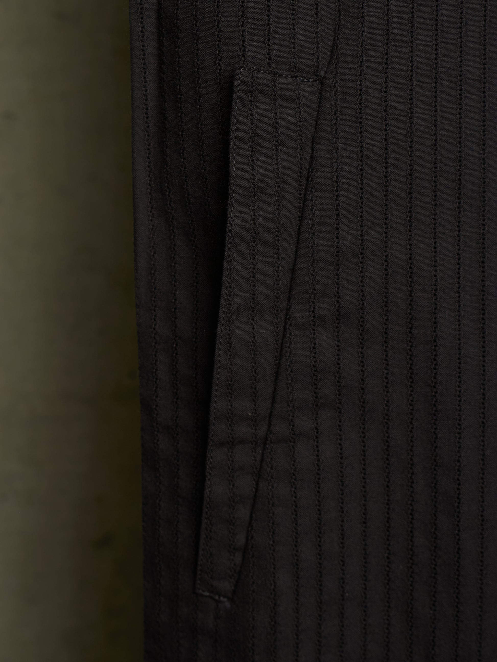 Close-up of a dark charcoal gray pinstriped fabric garment, showing a vertical pocket seam and fine stitched texture.