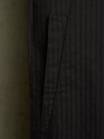 Close-up of a dark charcoal gray pinstriped fabric garment, showing a vertical pocket seam and fine stitched texture.