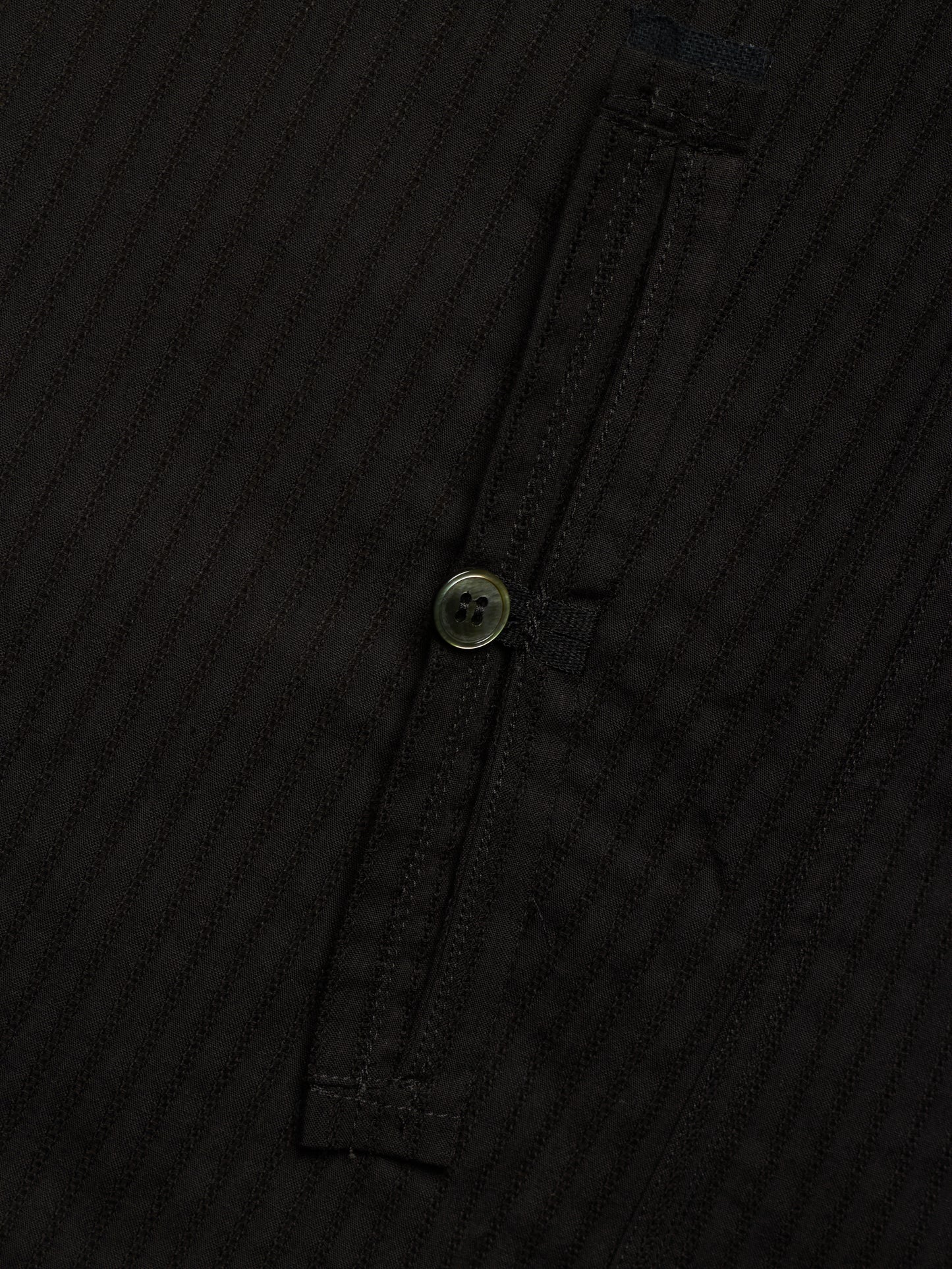 Close-up of a black ribbed fabric garment with a single button closure on a dark background.