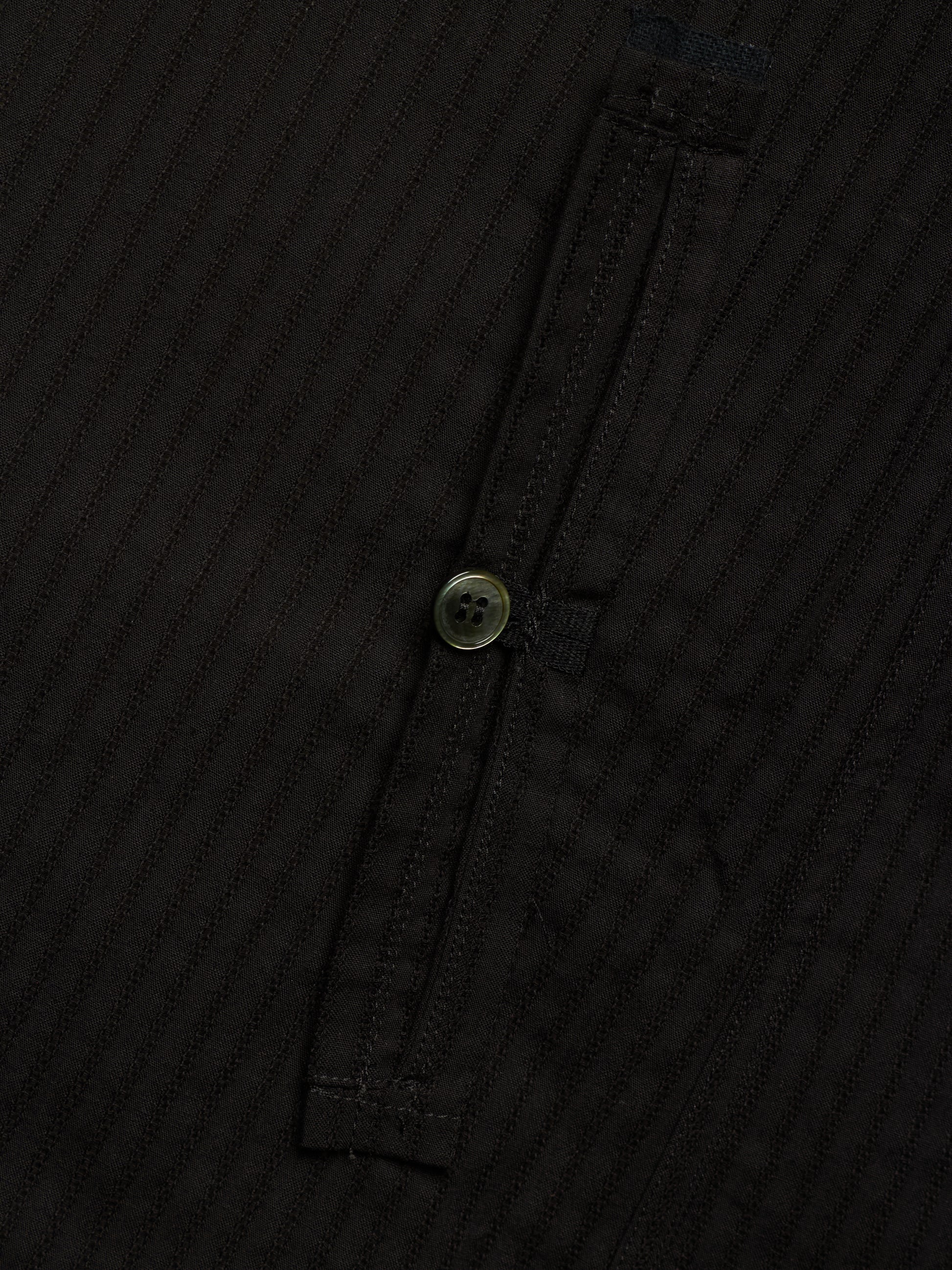 Close-up of a black ribbed fabric garment with a single button closure on a dark background.
