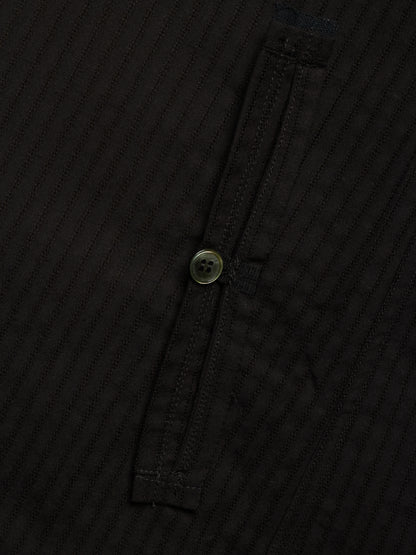 Close-up of a black ribbed fabric garment with a single button closure on a dark background.