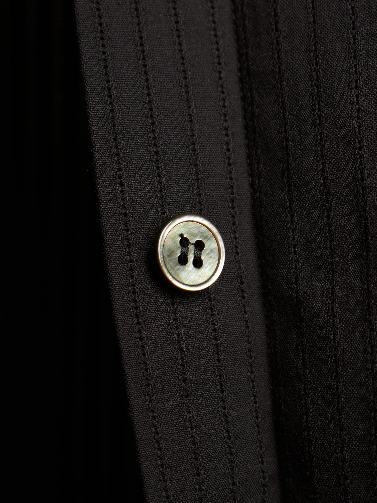 Close-up of a black pinstriped shirt with a round mother-of-pearl button with a gold-tone metal rim.