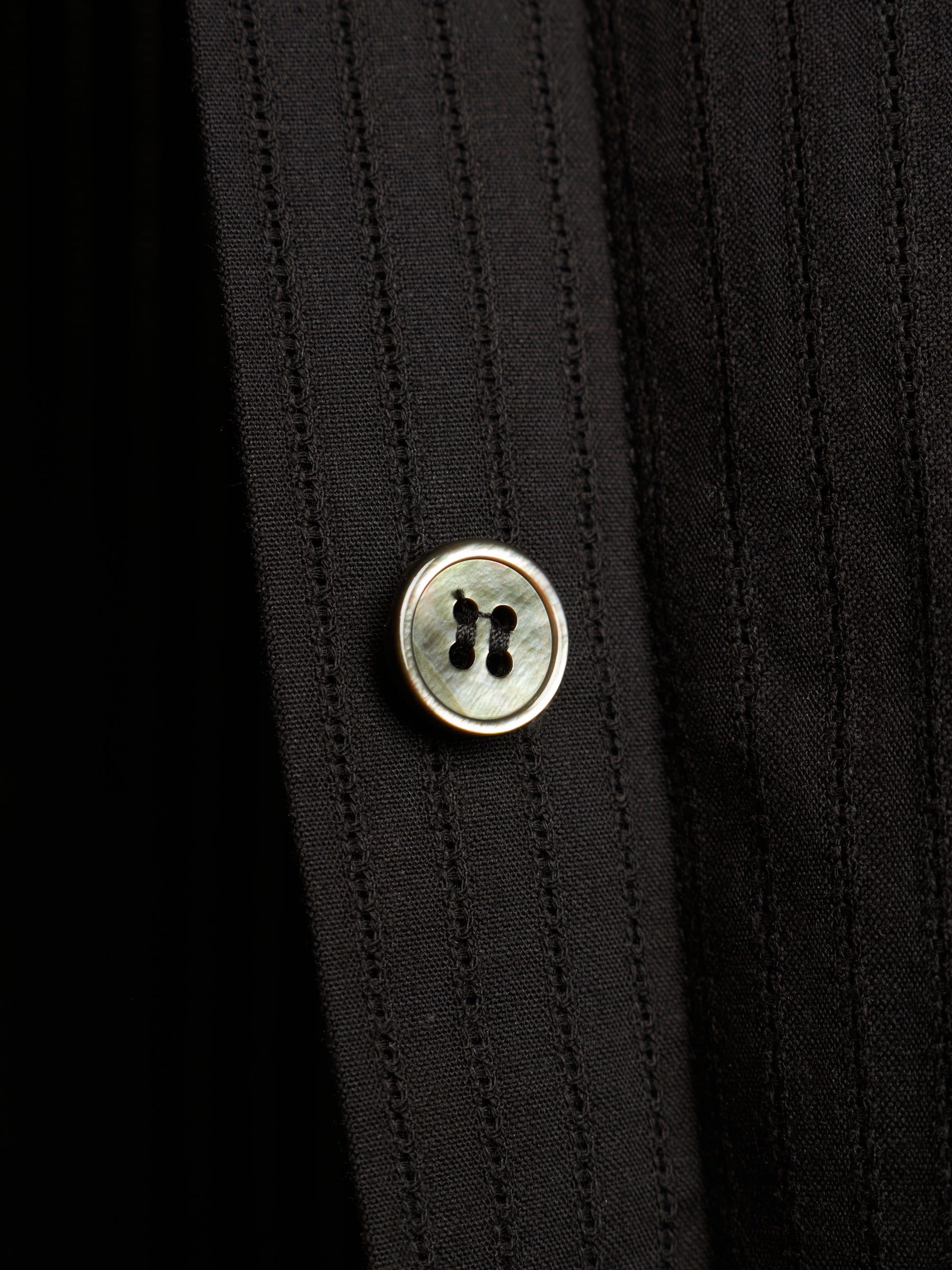 Close-up of a black pinstriped shirt with a round mother-of-pearl button with a gold-tone metal rim.