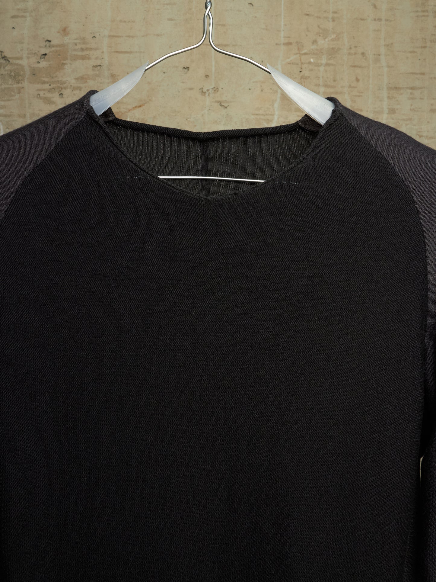 A black long-sleeve raglan shirt with dark gray sleeves, hanging on a white hanger against a light wood background.