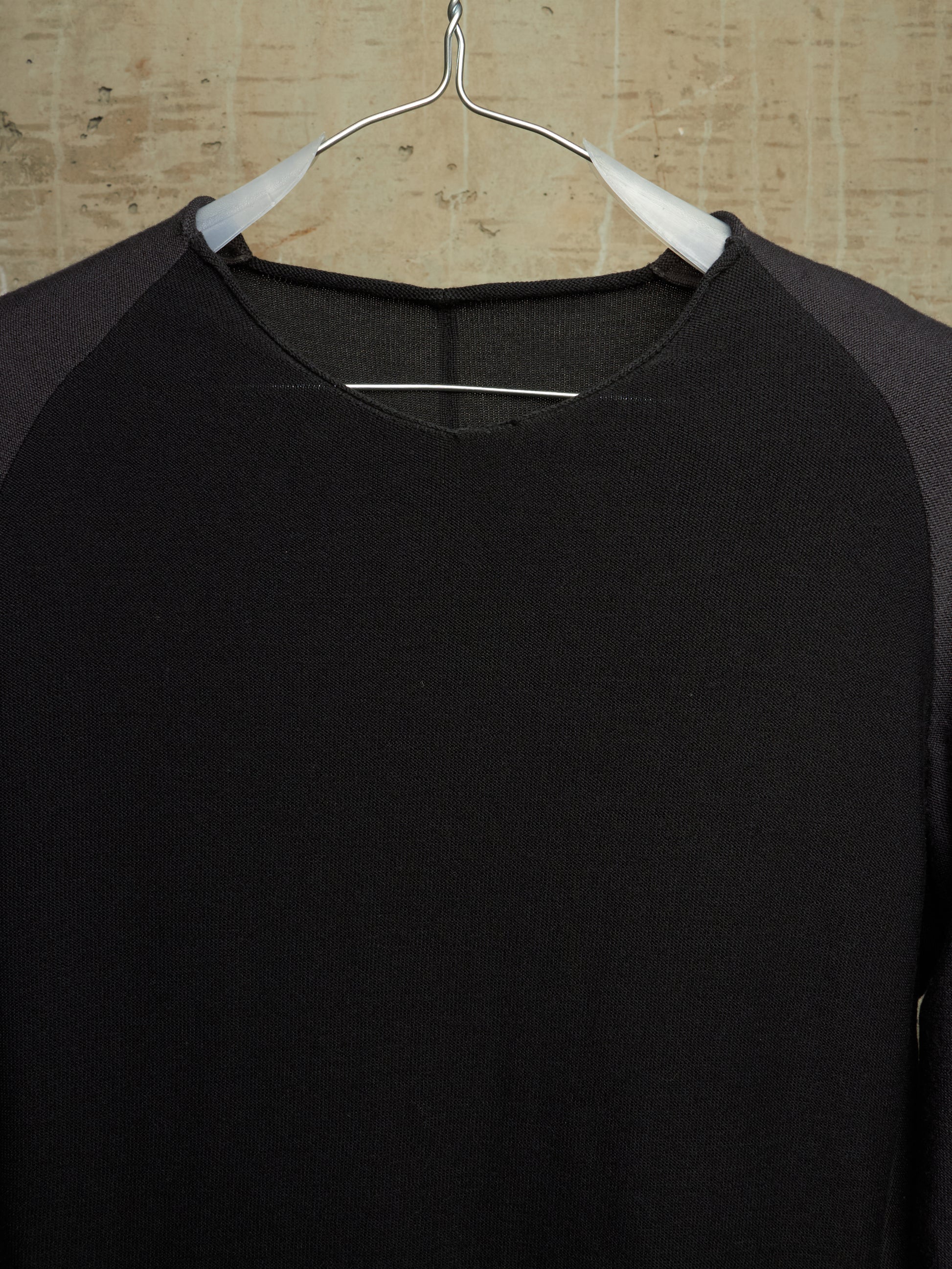 A black long-sleeve raglan shirt with dark gray sleeves, hanging on a white hanger against a light wood background.