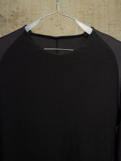 A black long-sleeve raglan shirt with dark gray sleeves, hanging on a white hanger against a light wood background.