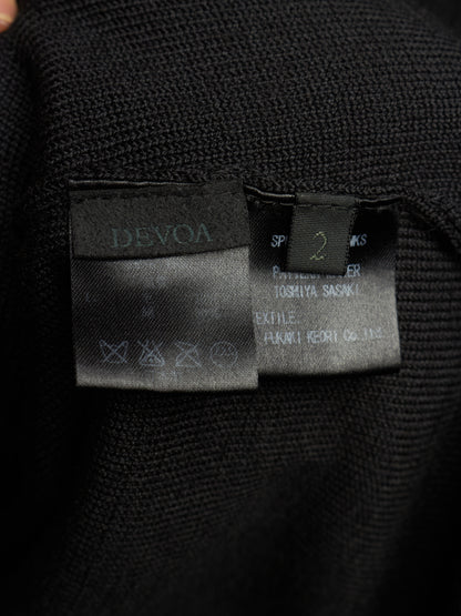Close-up of a black knit garment showing two interior labels: a larger Devoa label on the left and a smaller size/manufacturer label on the right.