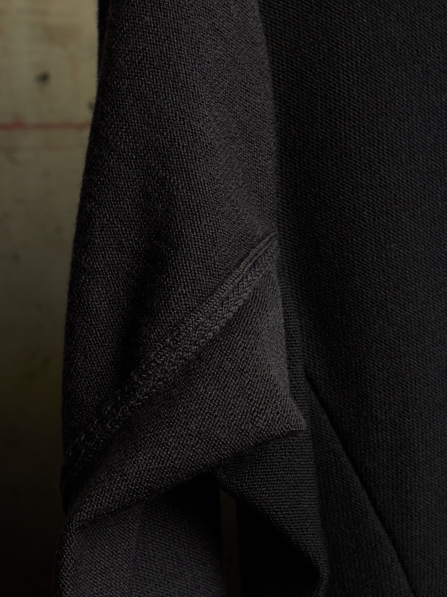 Close-up of a dark charcoal gray knit fabric, showing the fine texture and a diagonal seam.