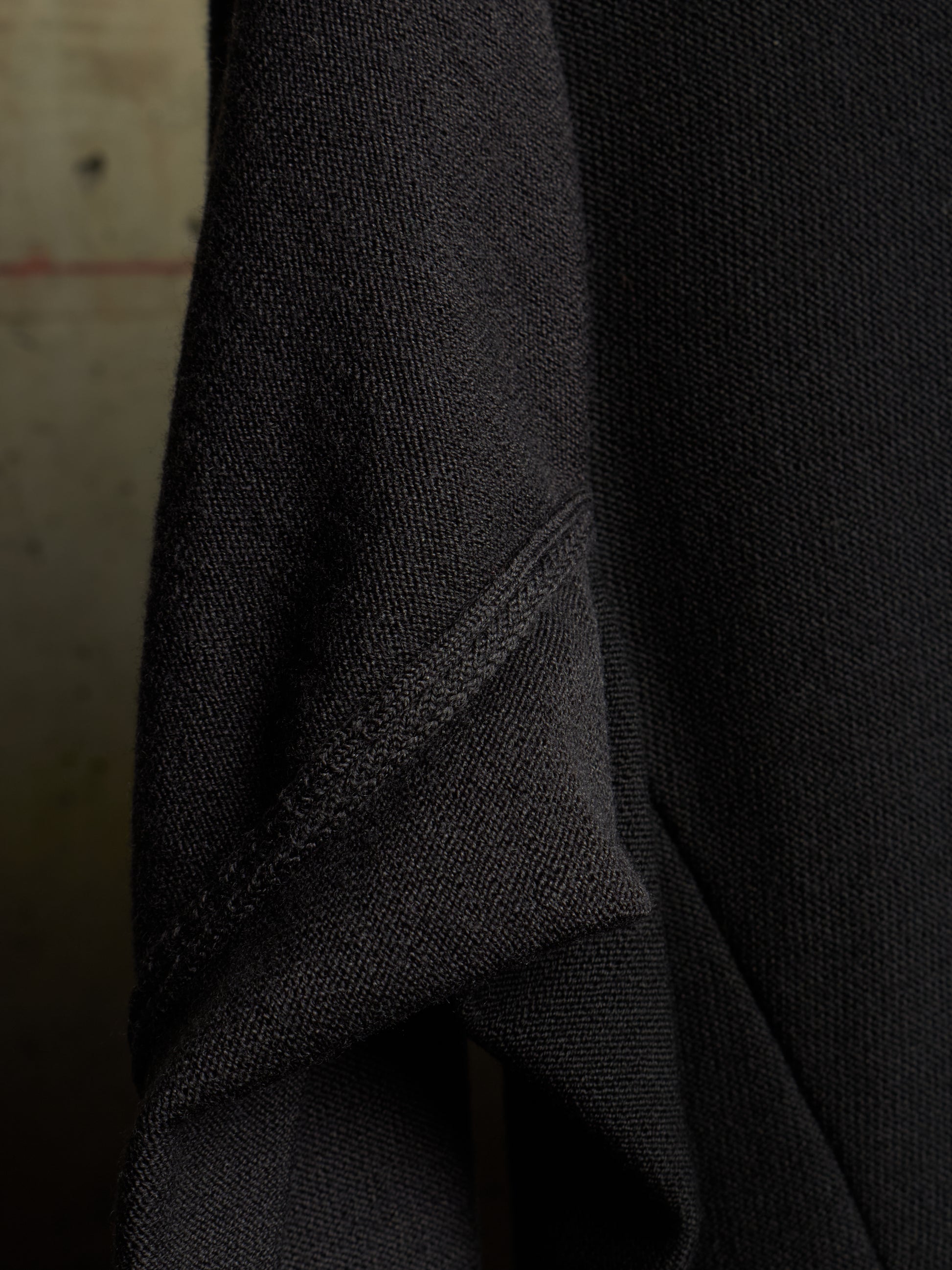 Close-up of a dark charcoal gray knit fabric, showing the fine texture and a diagonal seam.
