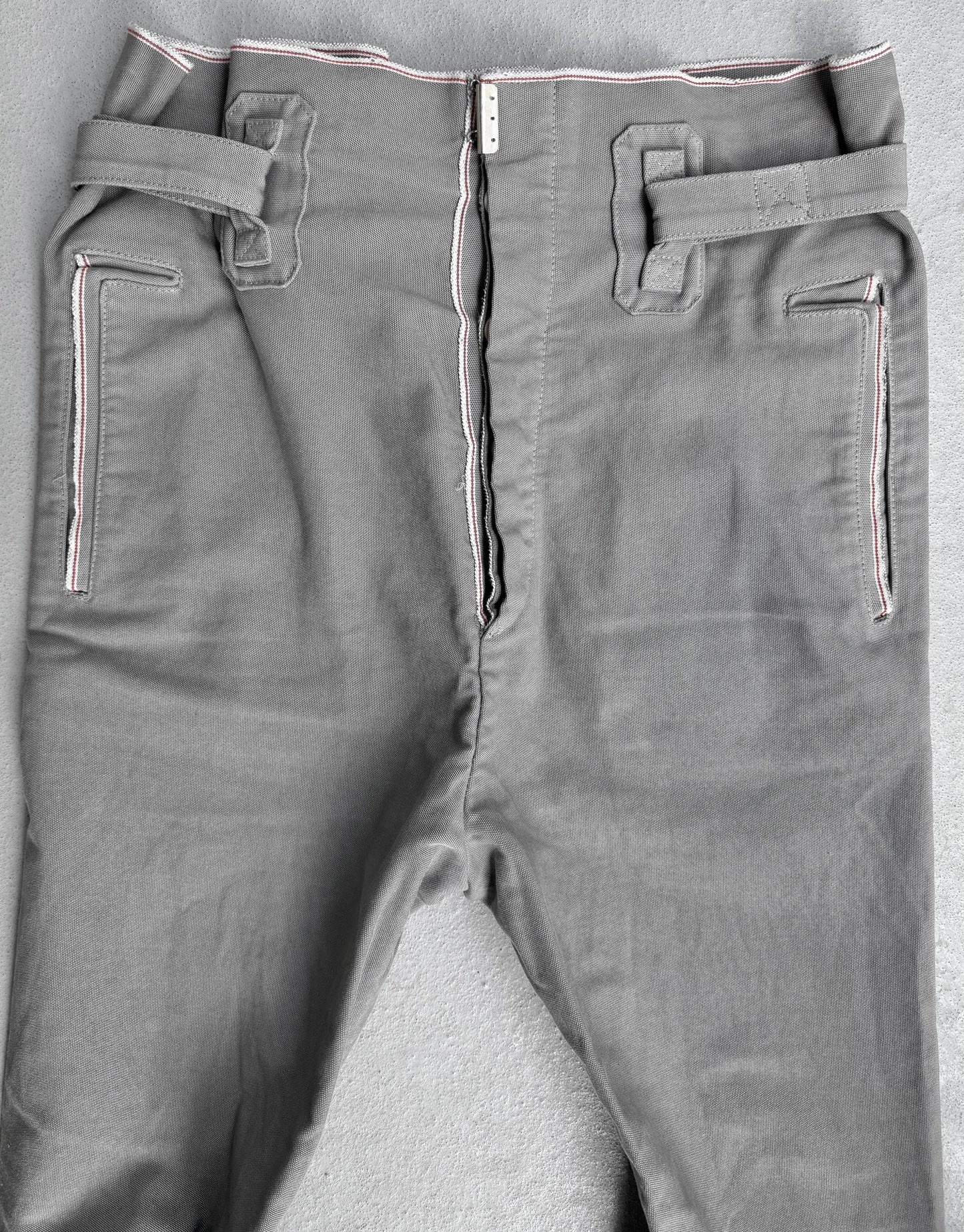 The Carol Christian Poell 2010 “IN-BETWEEN” PM/2578 PEDGE Self-edge High-waisted Metre Pants feature a partially undone zipper, white and pink stitching accents, and two unique rectangular belt loops per side, reflecting avant-garde design.