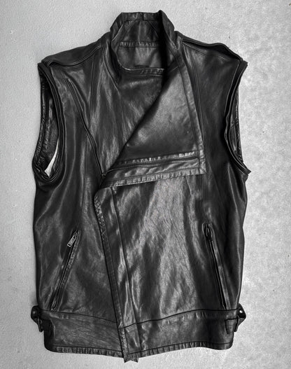 The Gareth Pugh AW09 Detachable Sleeves Horse Leather Riders Jacket, a sleeveless black piece with asymmetric front zip, wide lapel, side pockets, and adjustable hem straps, is displayed flat on a light gray surface.