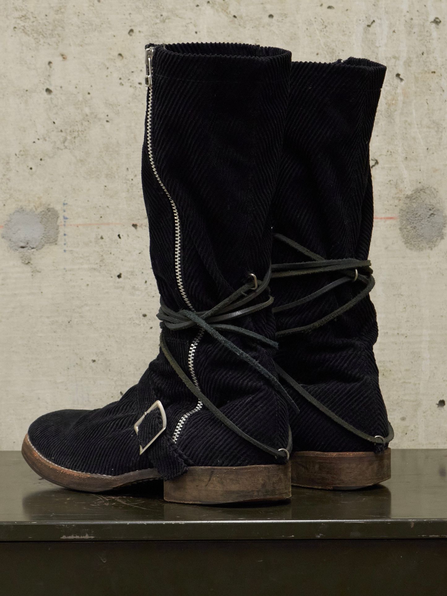 Pair of black corduroy boots with laces on a concrete surface