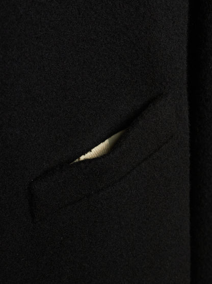 Close-up detail of a black wool or cashmere fabric garment, showing a sliver of a light beige or cream ribbed knit lining or pocket detail.