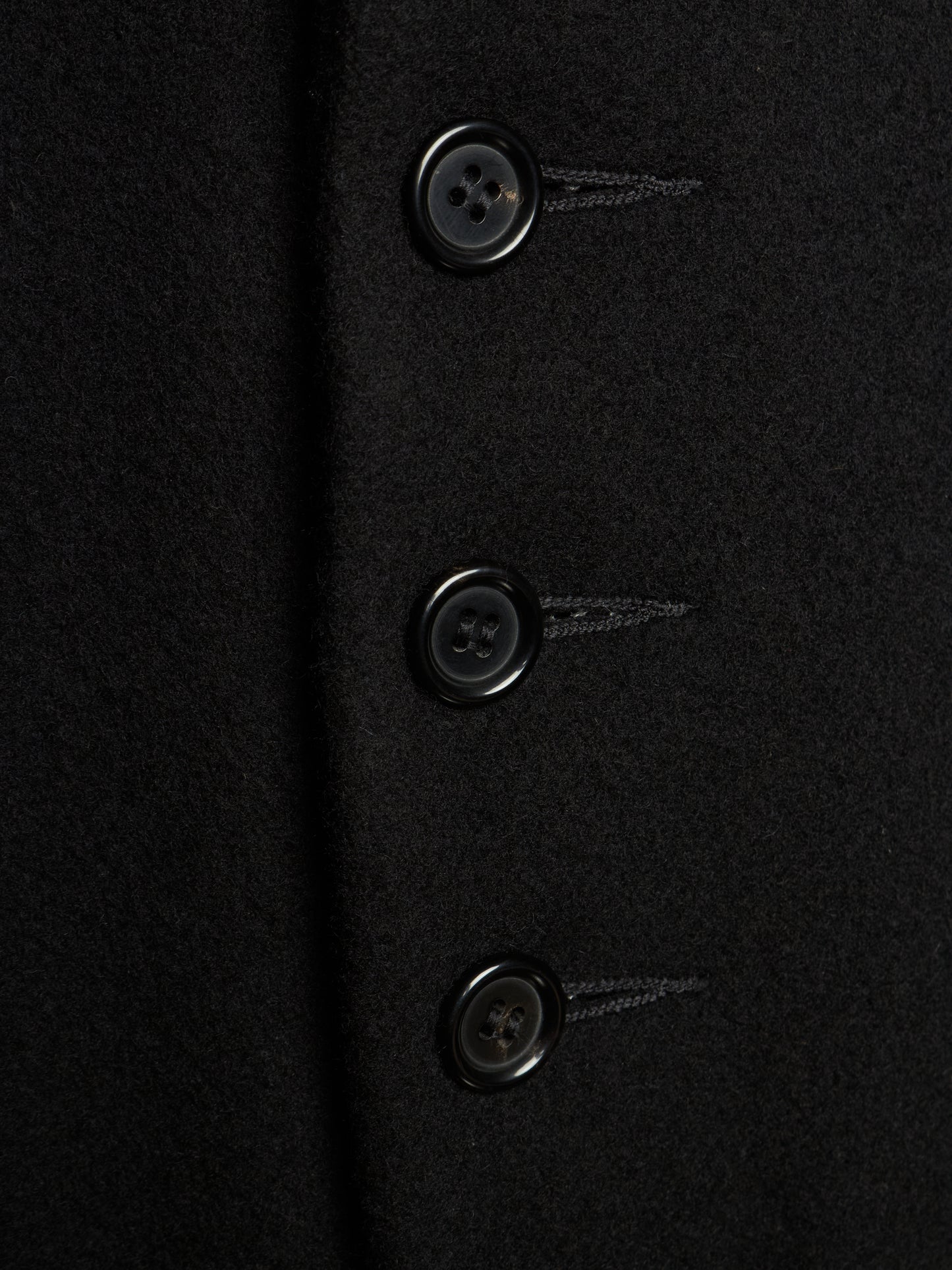 Close-up of a black wool-like fabric garment with three dark buttons aligned vertically.