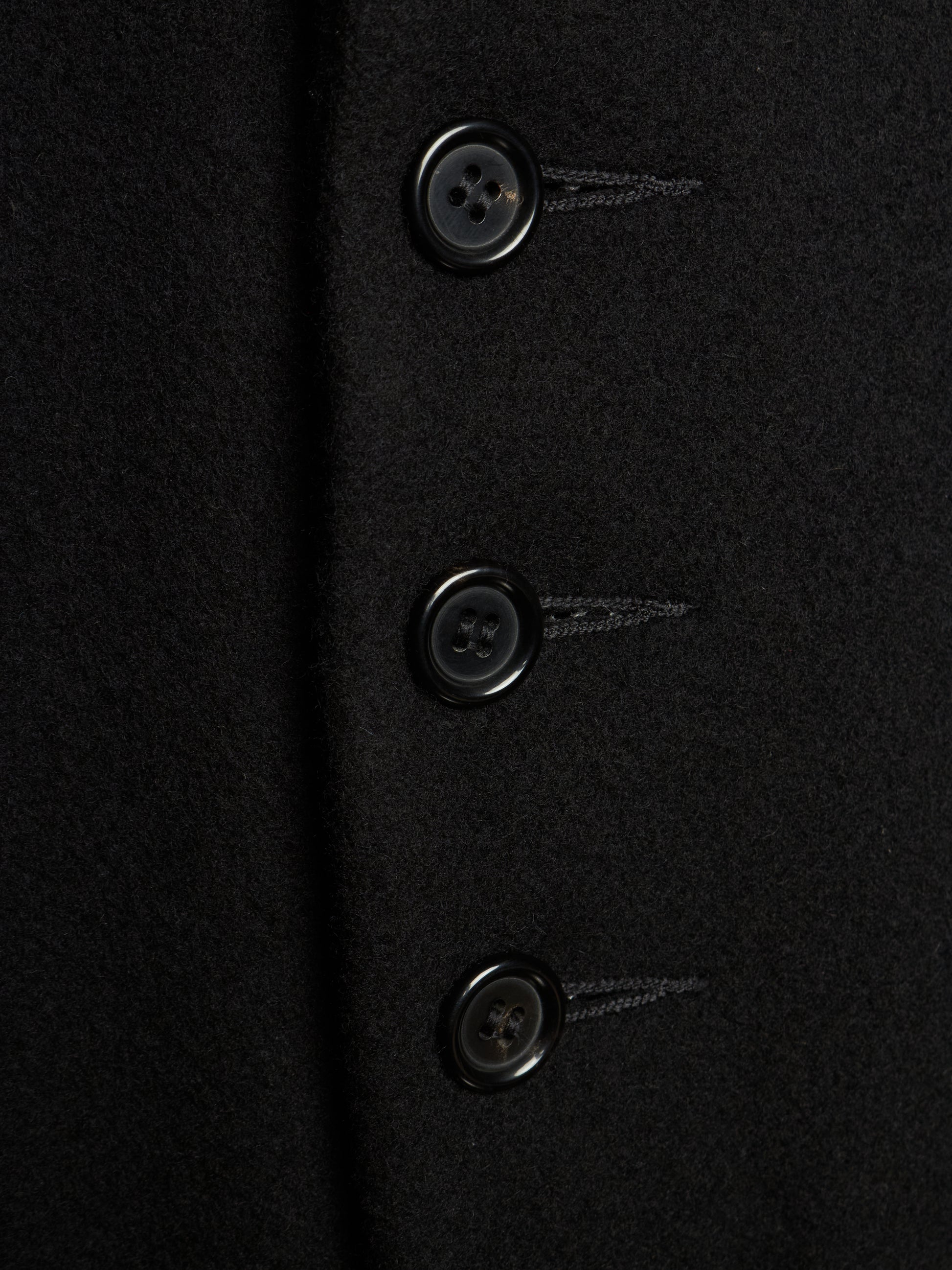 Close-up of a black wool-like fabric garment with three dark buttons aligned vertically.