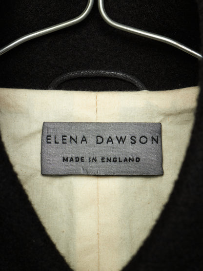 Close-up of the interior neck label of a black coat or sweater on a hanger, showing the brand 'Elena Dawson' and 'Made in England' on a cream-colored lining.