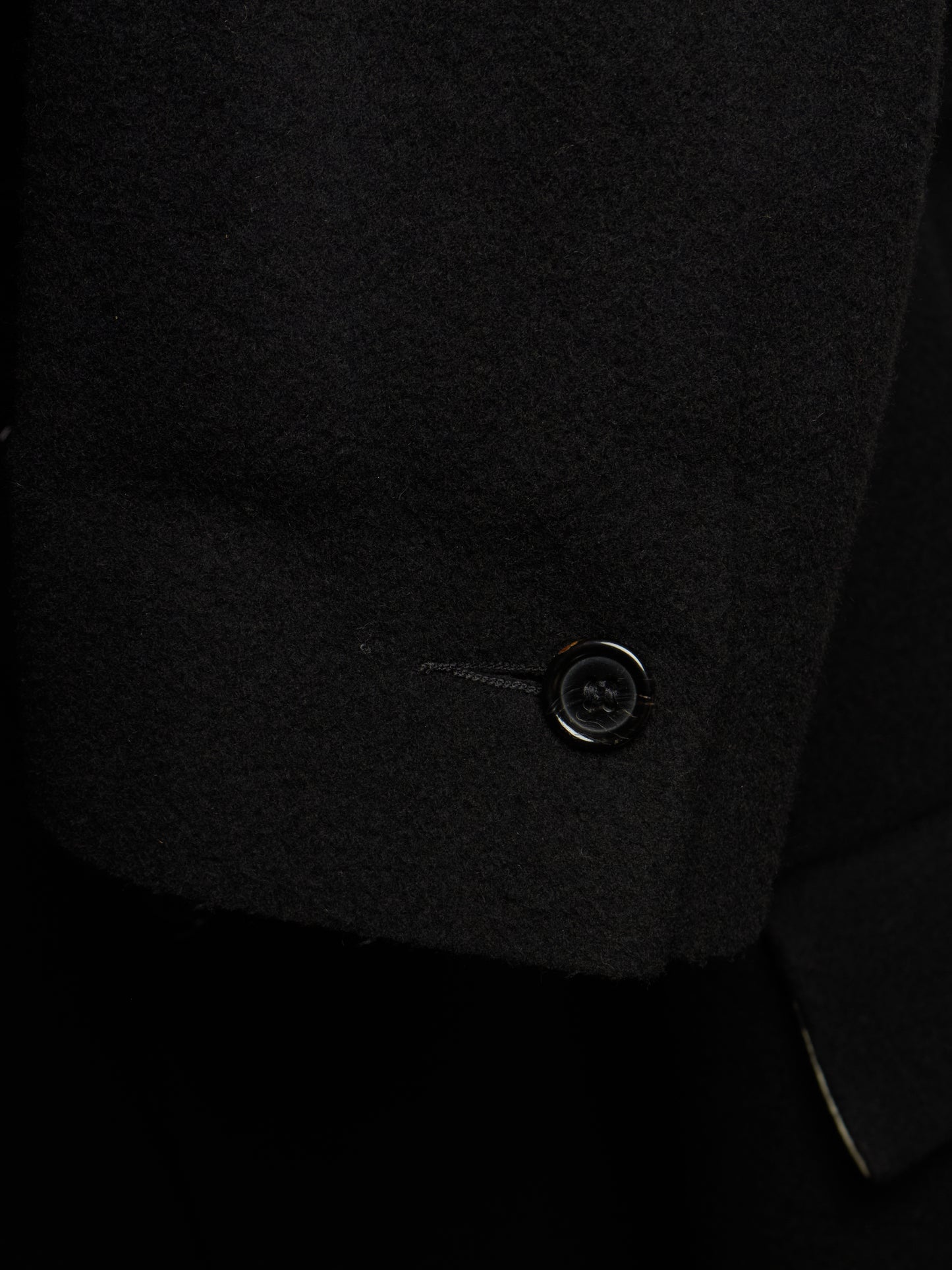Close-up detail of a black wool or cashmere blazer sleeve cuff, showing the texture of the fabric and a single black button.