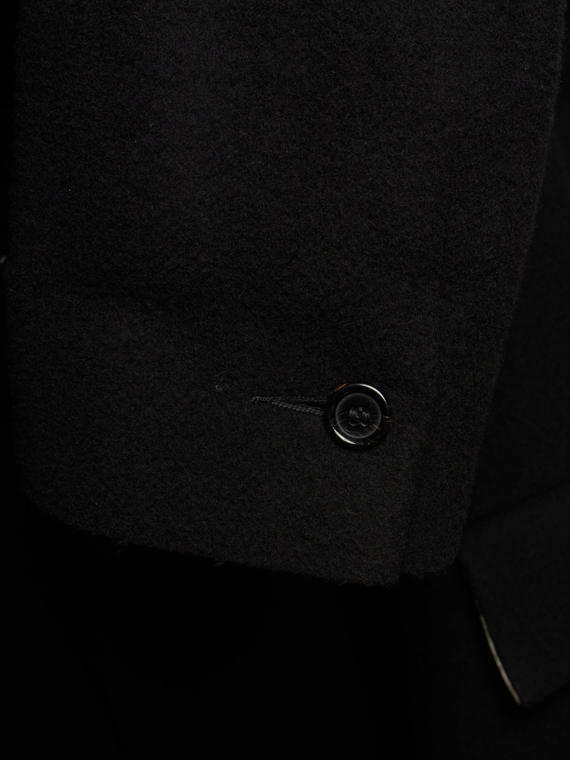 Close-up detail of a black wool or cashmere blazer sleeve cuff, showing the texture of the fabric and a single black button.